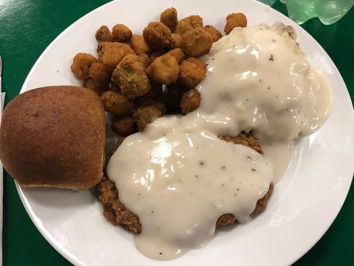 A plate of chicken-fried steak with cream gravy, fried okra and a roll