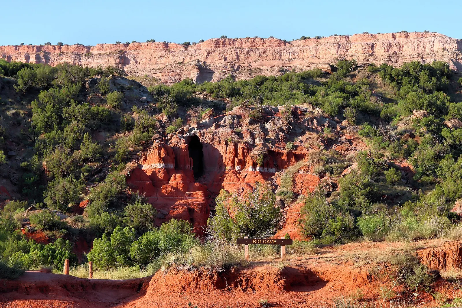 Red-rock bluff with a shallow cave above juniper slopes and a flat caprock rim
