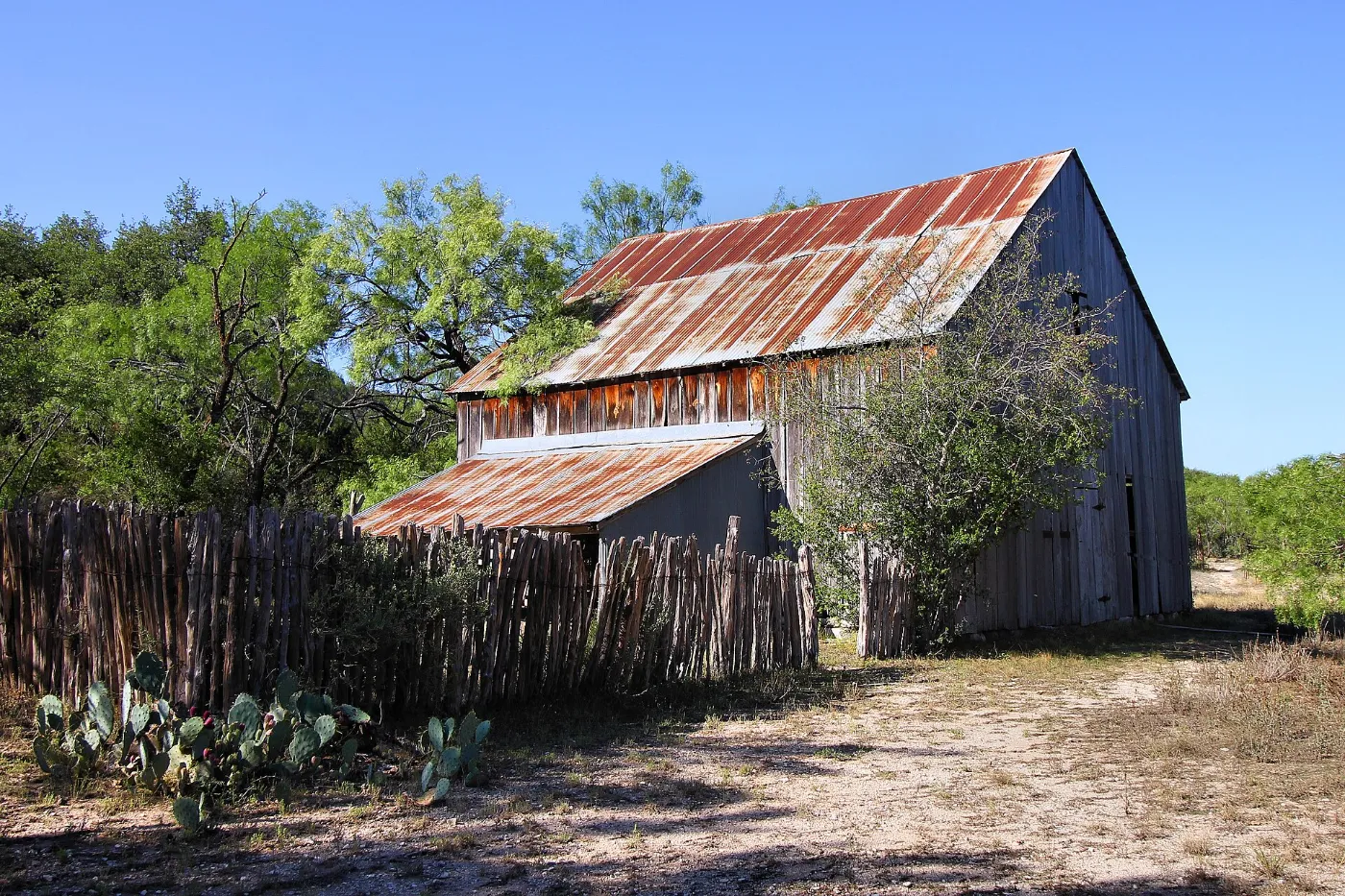 Old wooden barn with a rusted tin roof behind a cedar picket fence